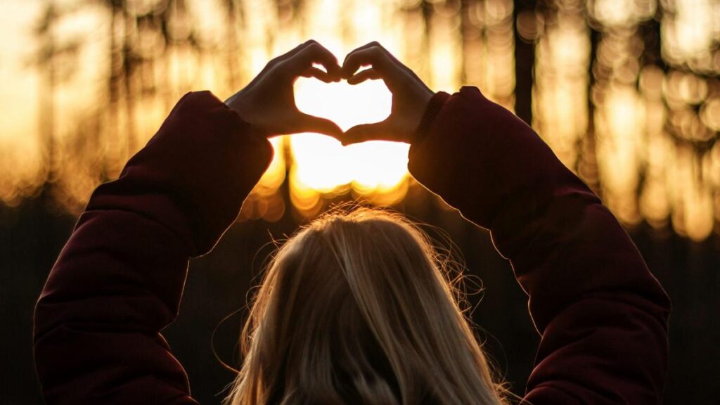 Hands forming a heart shape against a warm sunset during a reflective moment.